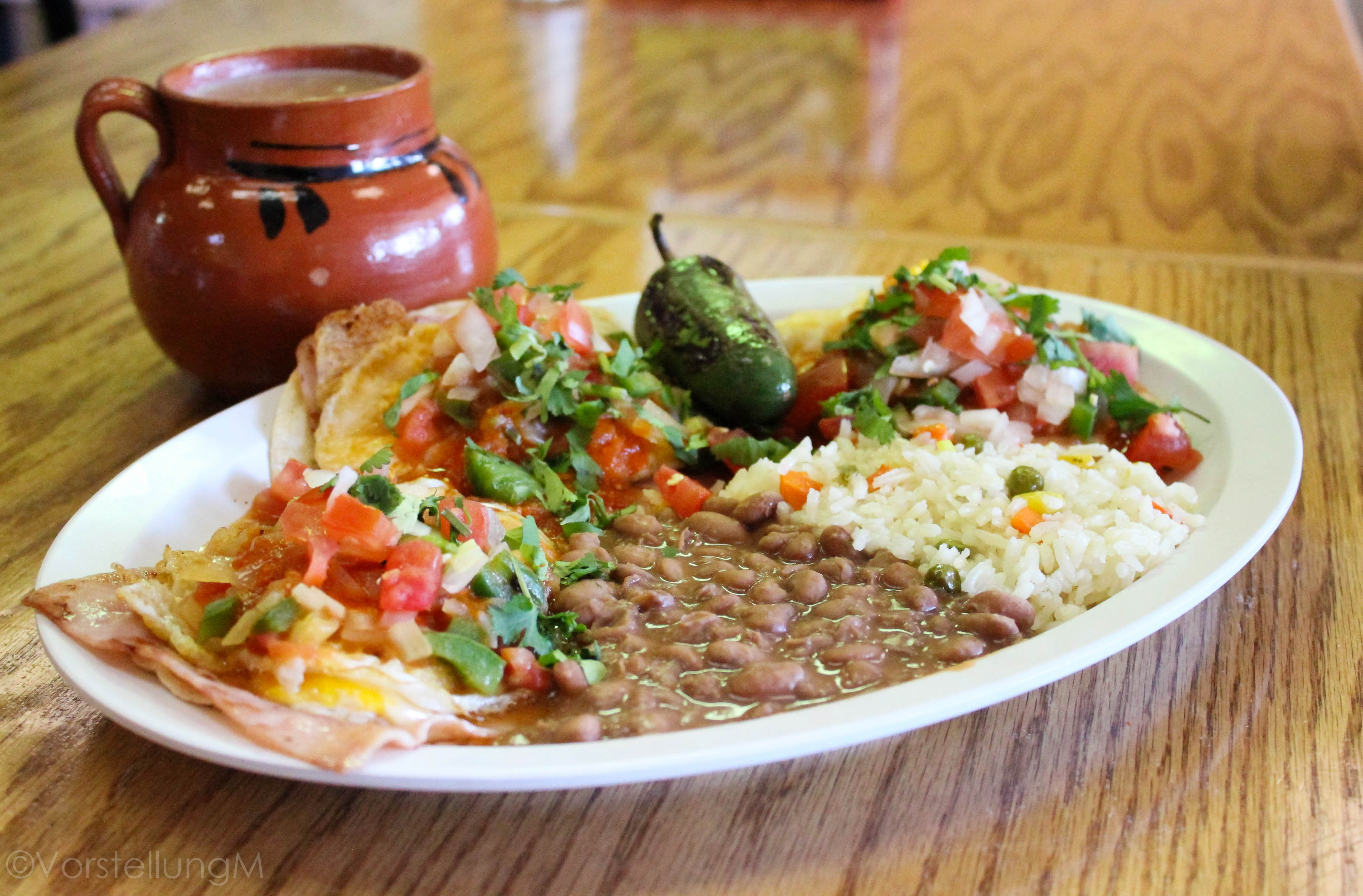 Champurrado en taza de barro, con un plato de huevos rancheros con jamón, tomate, frijoles, arroz, pico de gallo, y un chile asado.